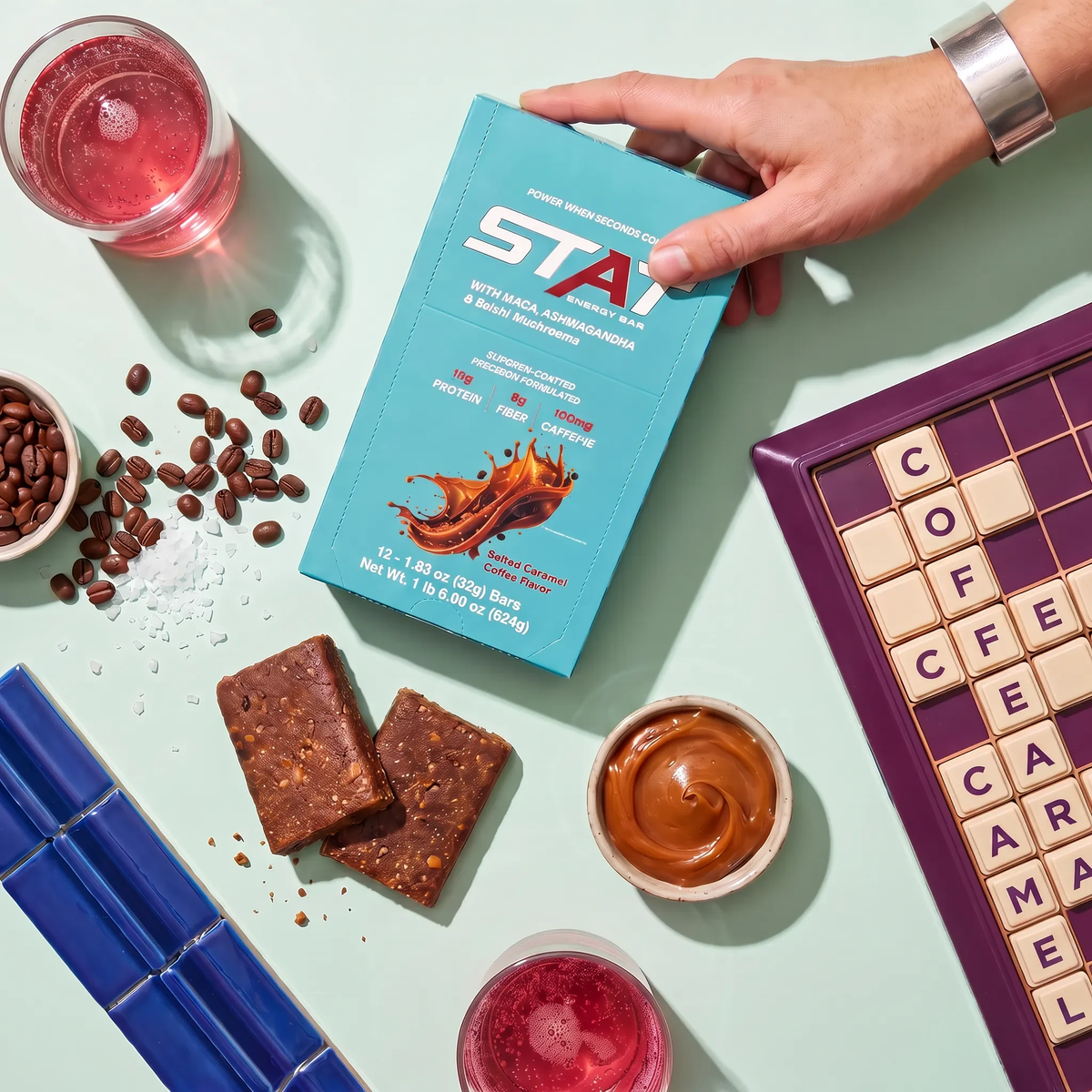 Hand placing a STAT Salted Caramel Coffee 12-count box on a table with bar pieces and coffee beans