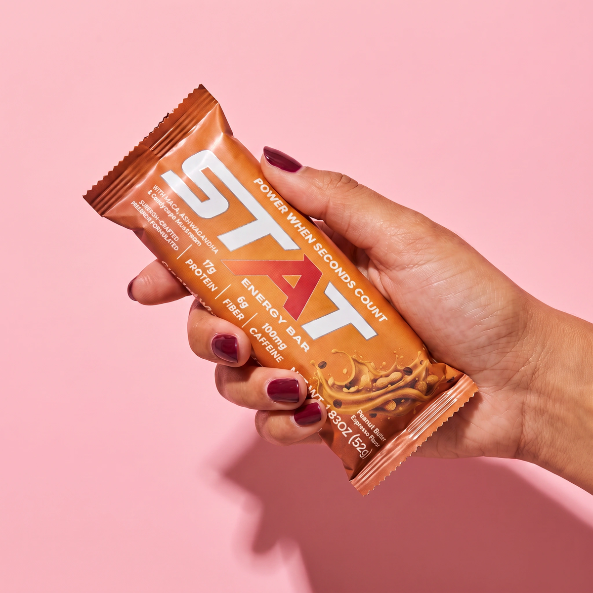 Hand holding a wrapped STAT Peanut Butter Espresso bar on a pink background