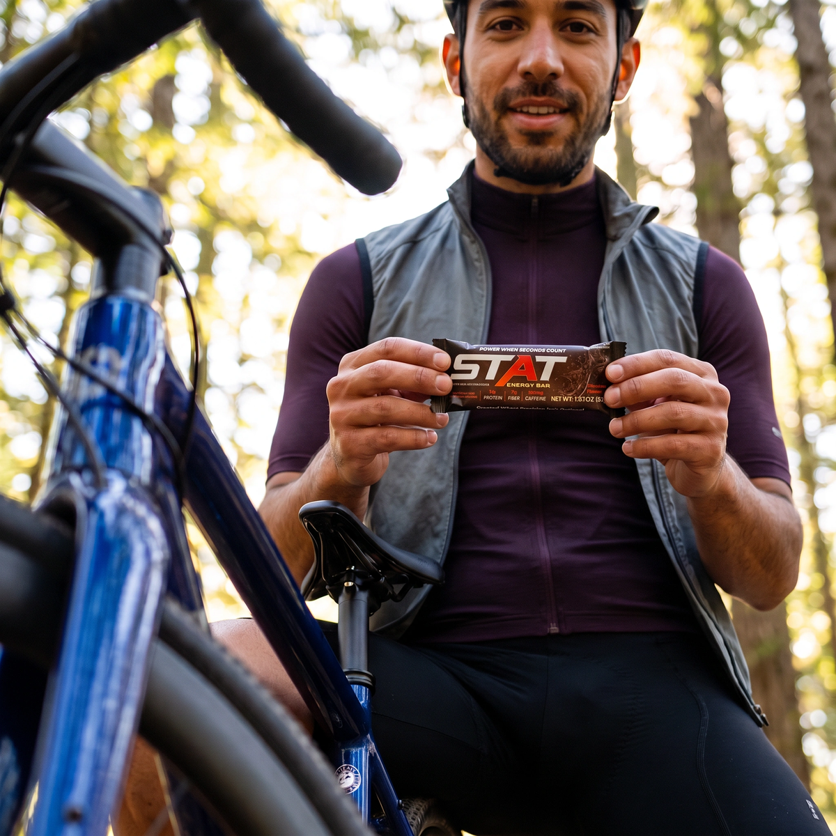Cyclist holding a wrapped STAT Chocolate bar beside his bike